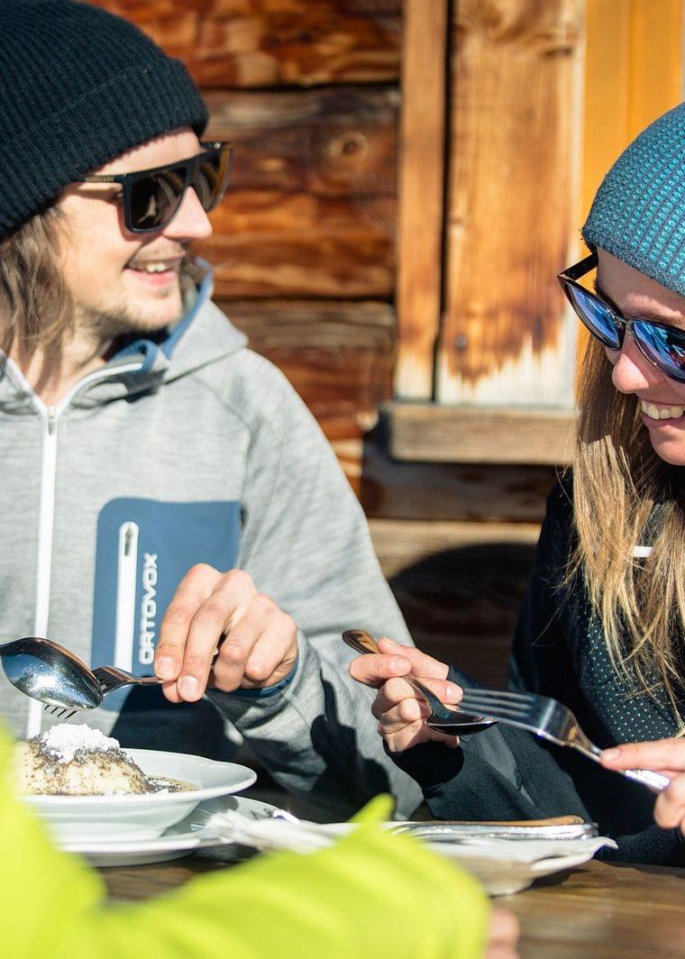 Friends in winter clothing sharing dessert outdoors at a mountain hut